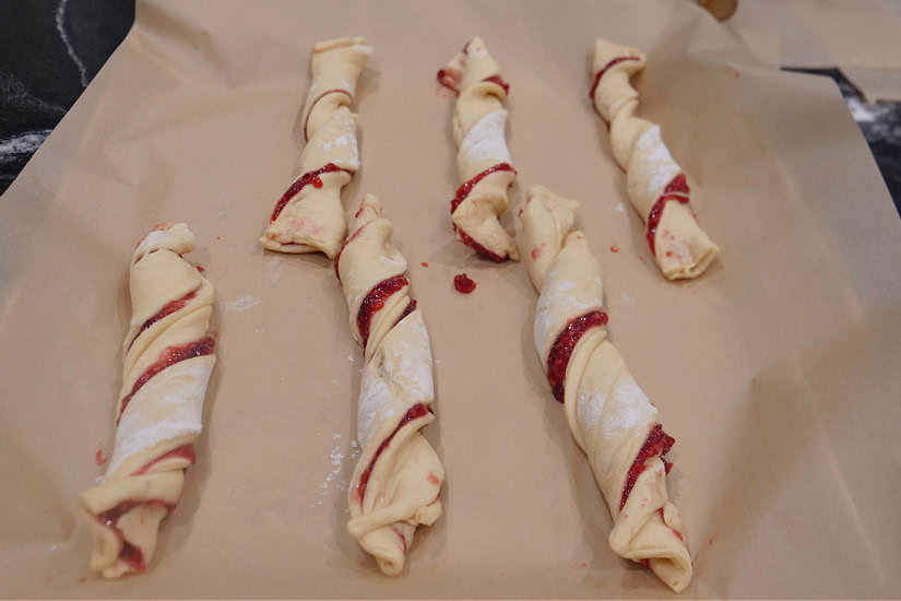 A baking sheet with parchment paper with twisted raspberry twists on it before being baked.