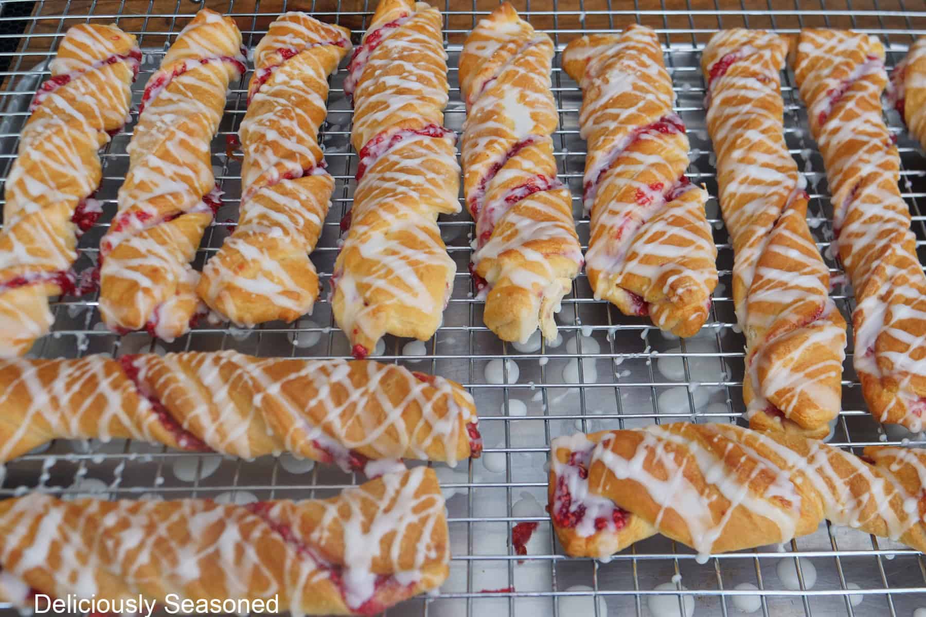 A wire rack with baked raspberry twists with lemon glaze drizzled over the tops.