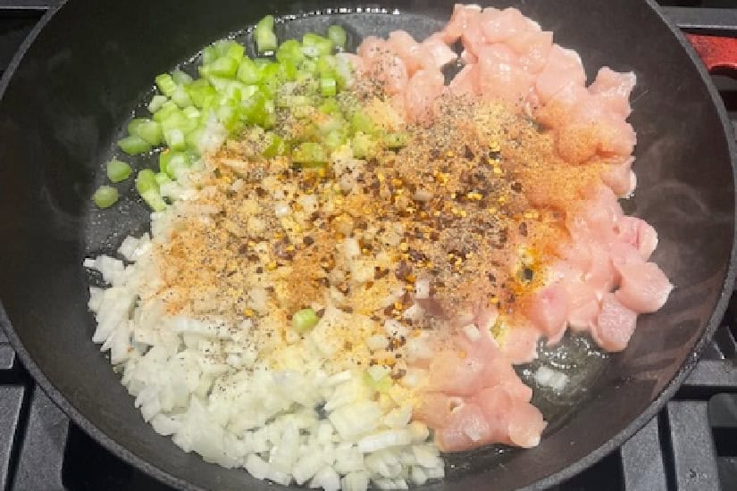 A pan with diced chicken, onions, celery and seasonings in it.