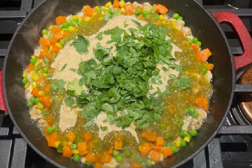A pan with chicken and all the ingredients needed to make the filling for salsa verde chicken pot pie.