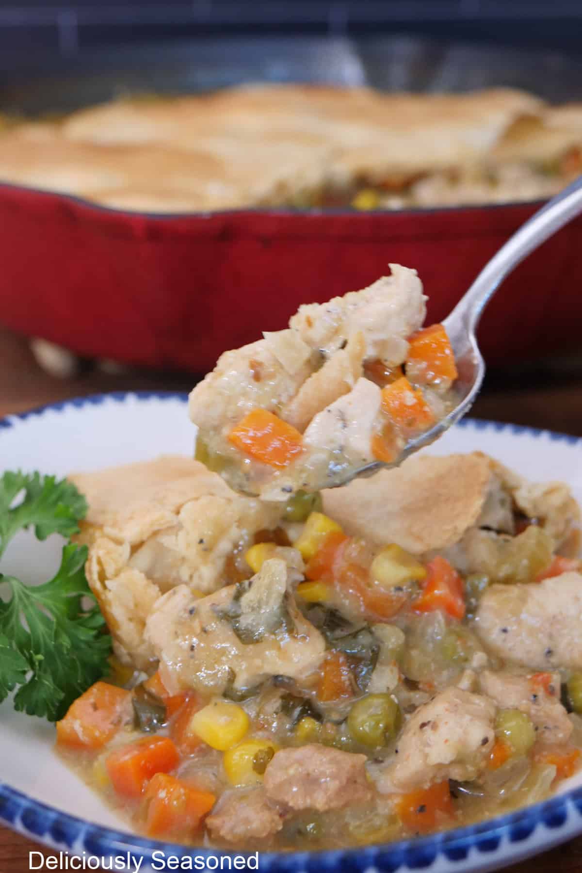 A spoonful of chicken pot pie held above a bowl with a serving in it.