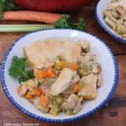 A wood surface with a round white bowl with blue trim filled with a serving of salsa verde chicken pot pie in it.