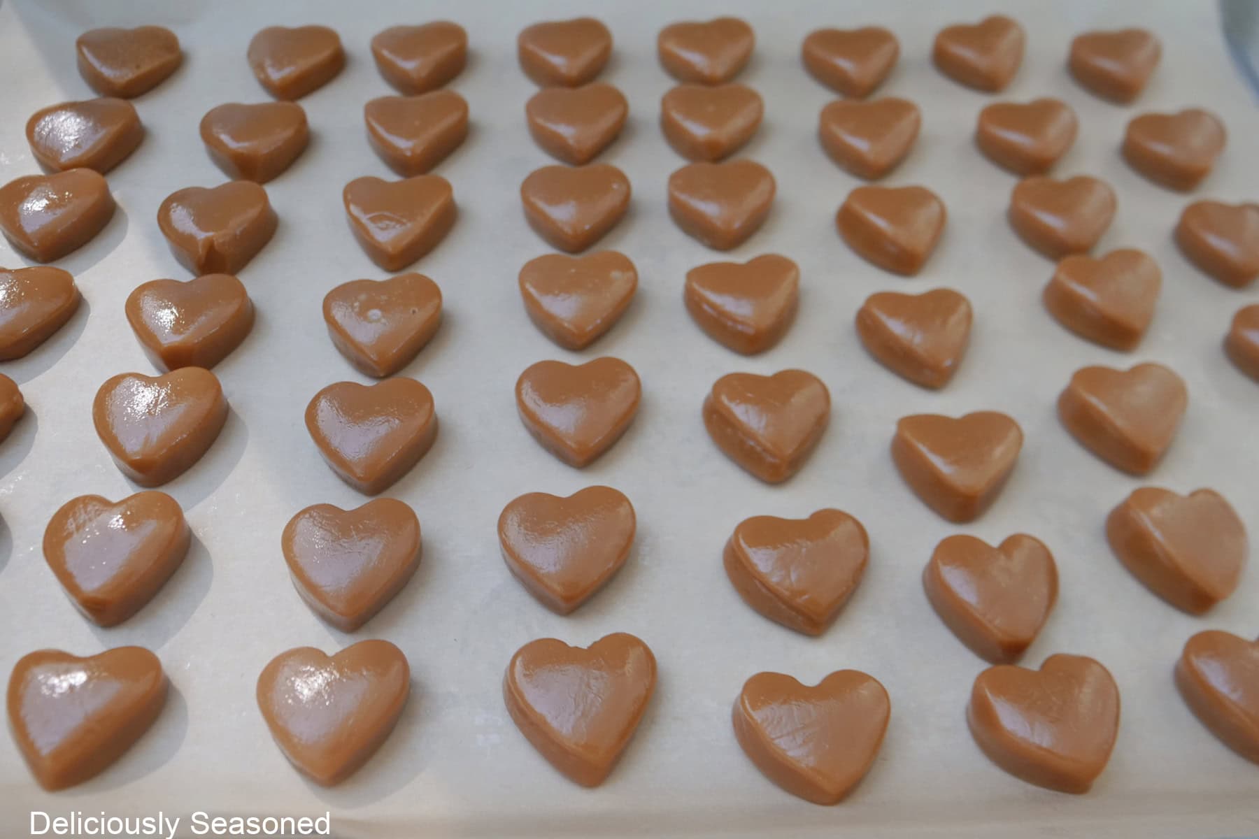 A baking sheet lined with parchment paper with little heart-shaped caramels on it.