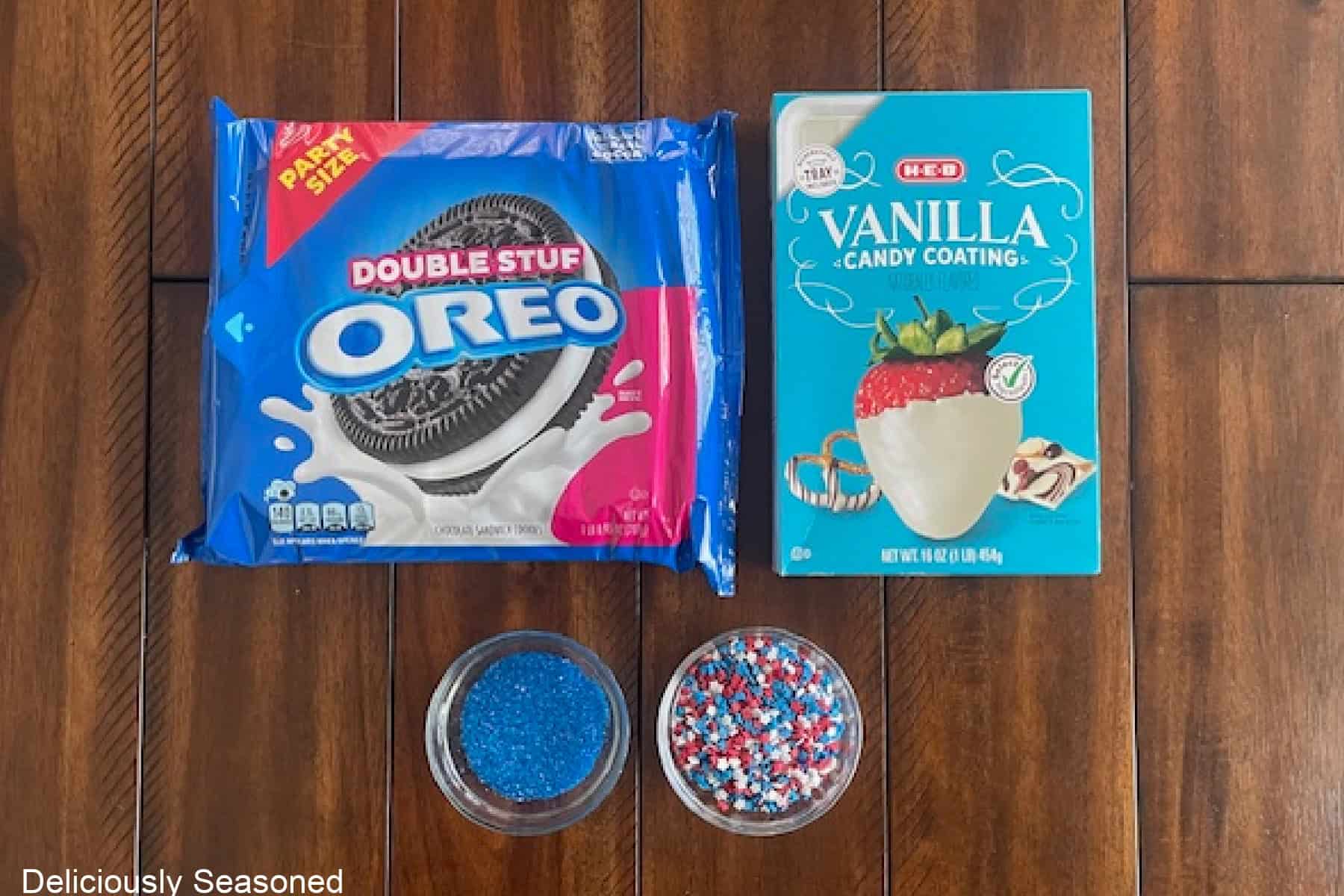 A wood surface with Oreo cookies, melting white chocolate, and two kinds of candy sprinkles on it.
