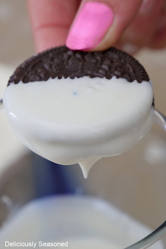 An Oreo cookie being dipped halfway into melted white chocolate.