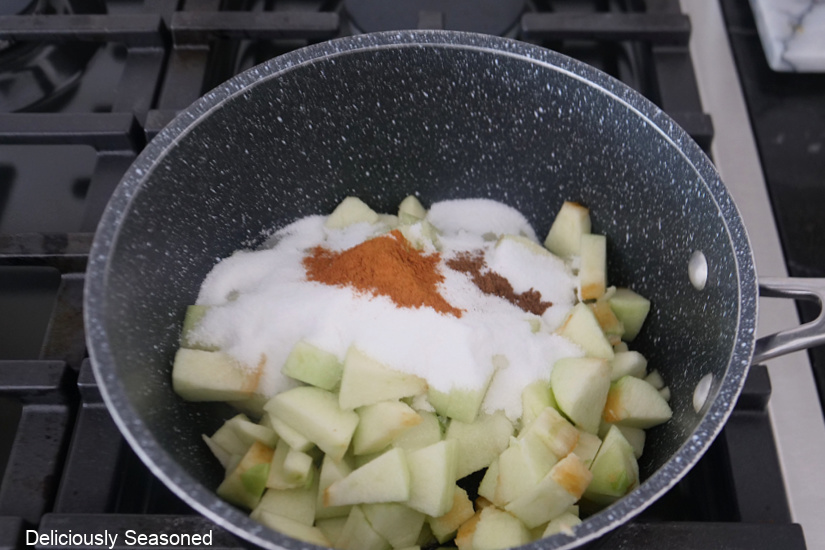A saucepan with chopped apples, sugar, cinnamon, and allspice in it.