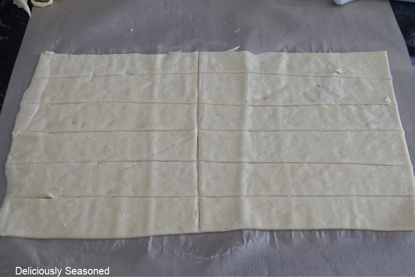 A piece of parchment paper with crescent dough on it rolled out and cut into 12 strips.