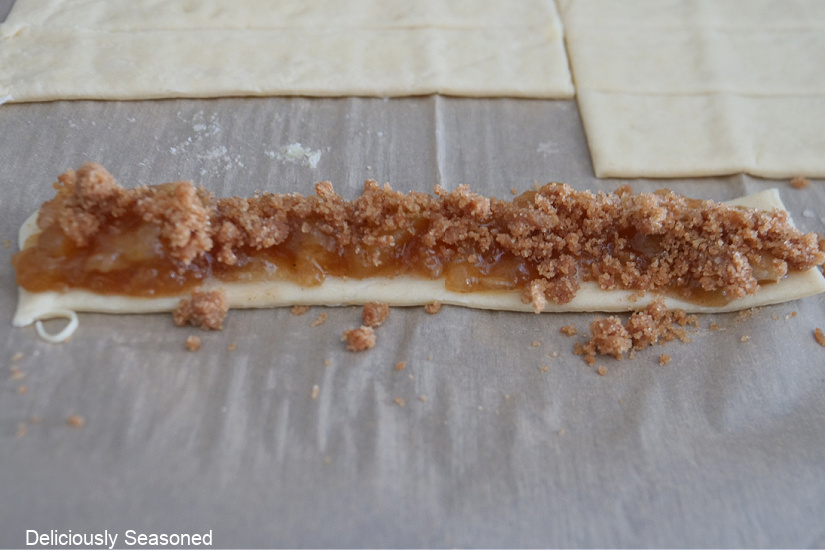 A crescent dough strip with apple filling and streusel on top of the apple filling.