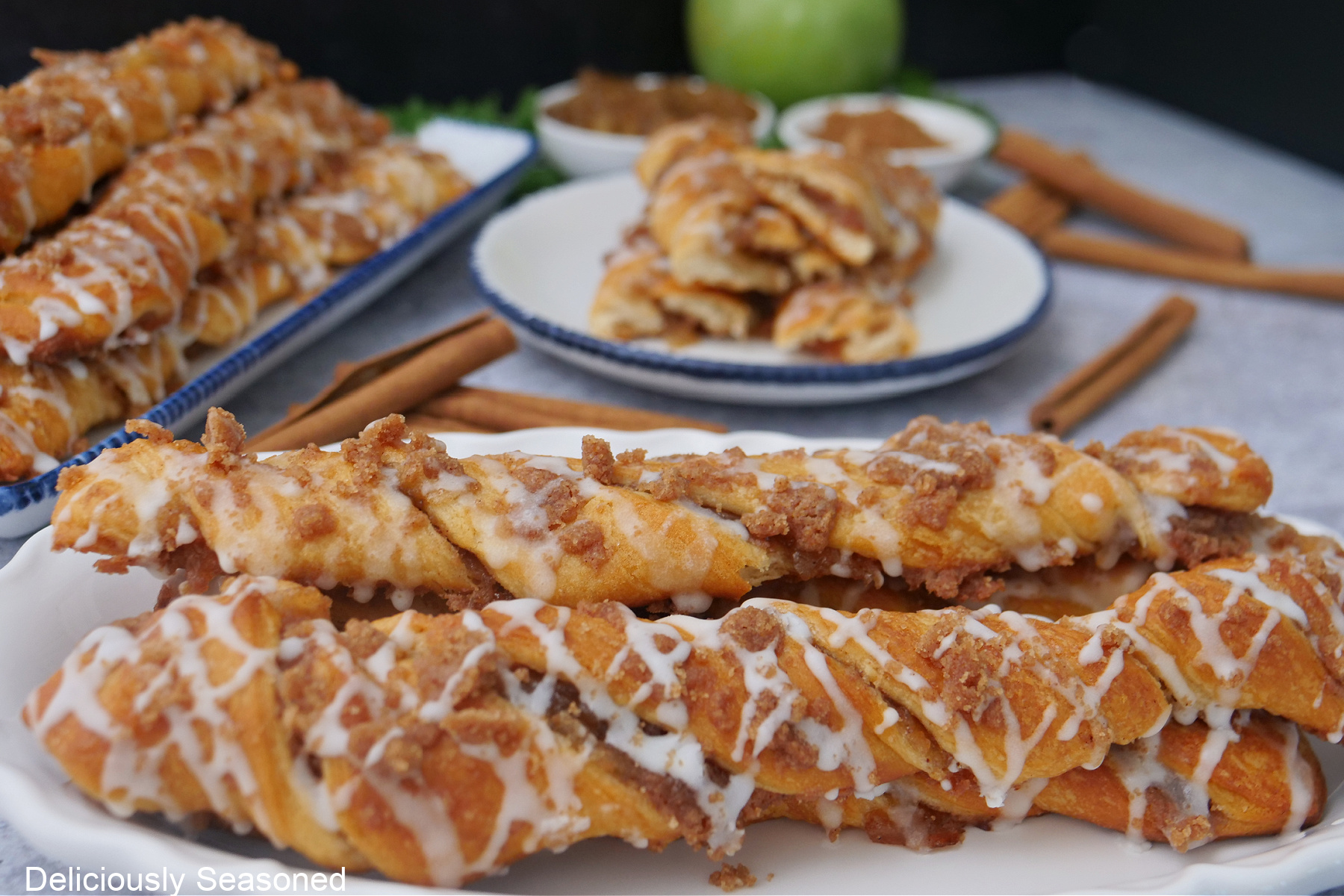 A wood surface with three white plates with blue trim with apple streusel twists on them