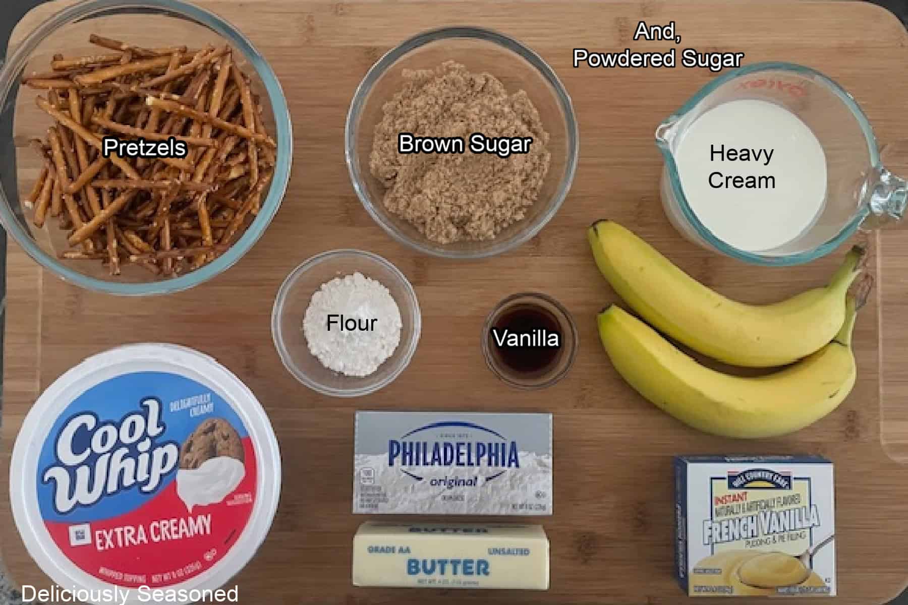 A wood surface with all the ingredients on it to make banana pudding pretzel dessert.