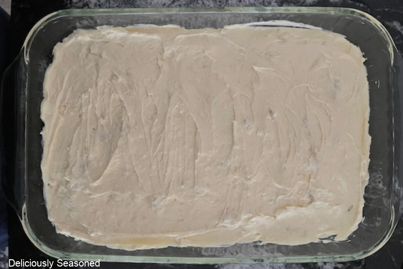 A black surface with a glass 9x13 baking dish filled with banana pudding mixture.