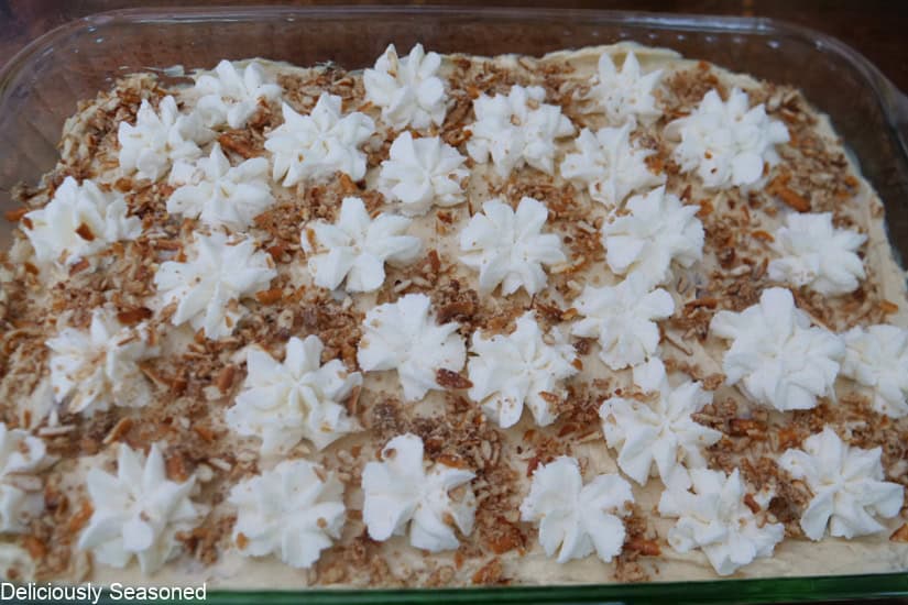 A glass baking dish with banana pudding pretzel dessert in it and it is topped with homemade whipped cream and a pretzel mixture.