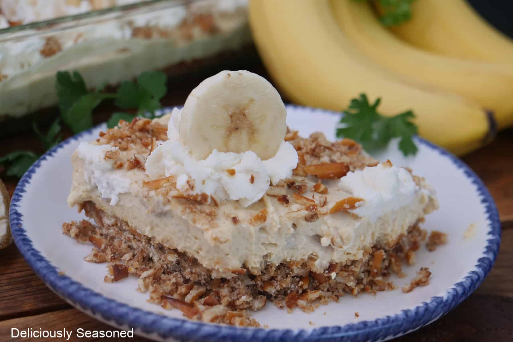 A white round plate with blue trim with a slice of banana pudding pretzel dessert on it.