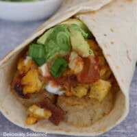A grey surface with a breakfast burrito placed on it showing the inside ingredients of the burrito.
