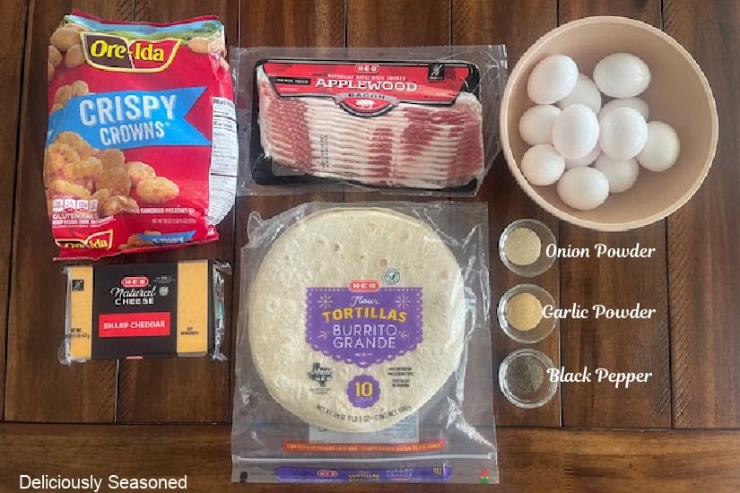 A wood table with all the ingredients to make breakfast burritos on it.
