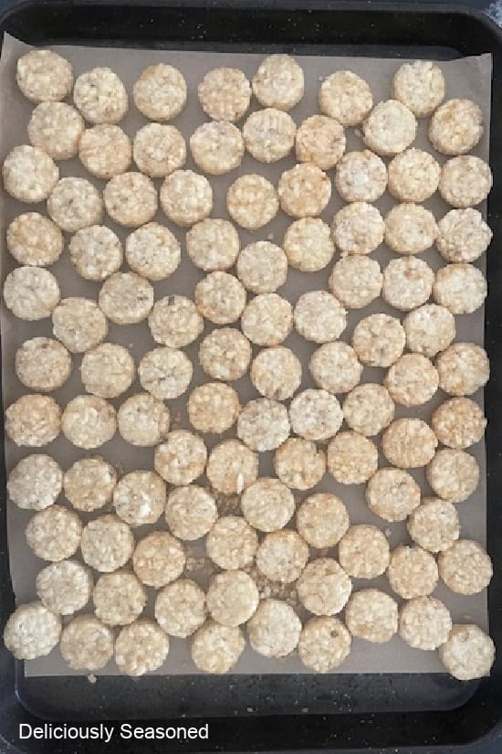 A baking sheet lined with parchment paper with tater tot rounds on it before going in the oven.