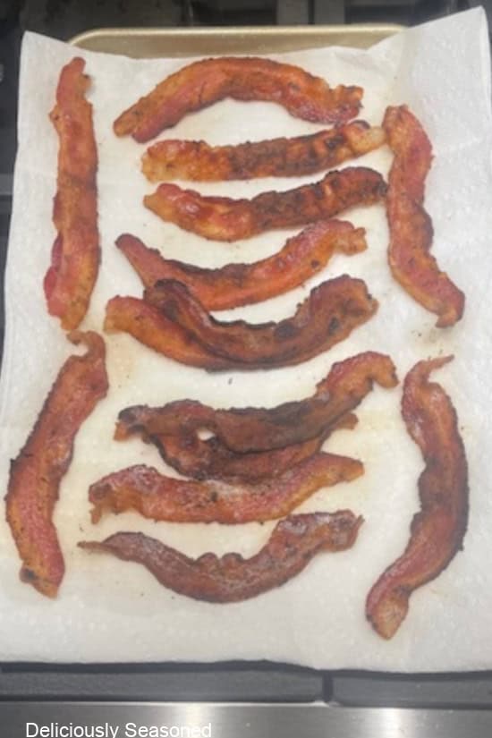 A baking sheet lined with paper towels and pieces of fried crispy bacon on it.