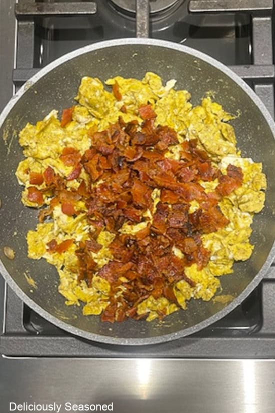 A frying pan with scrambled eggs and crumbled bacon in it.