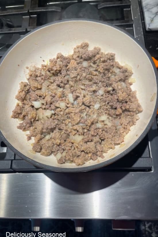 A cast-iron pan with cooked ground beef, Italian sausage, and onions in it.