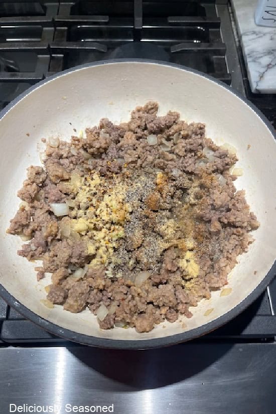 A cast-iron pan with cooked meat topped with seasonings and minced onions.