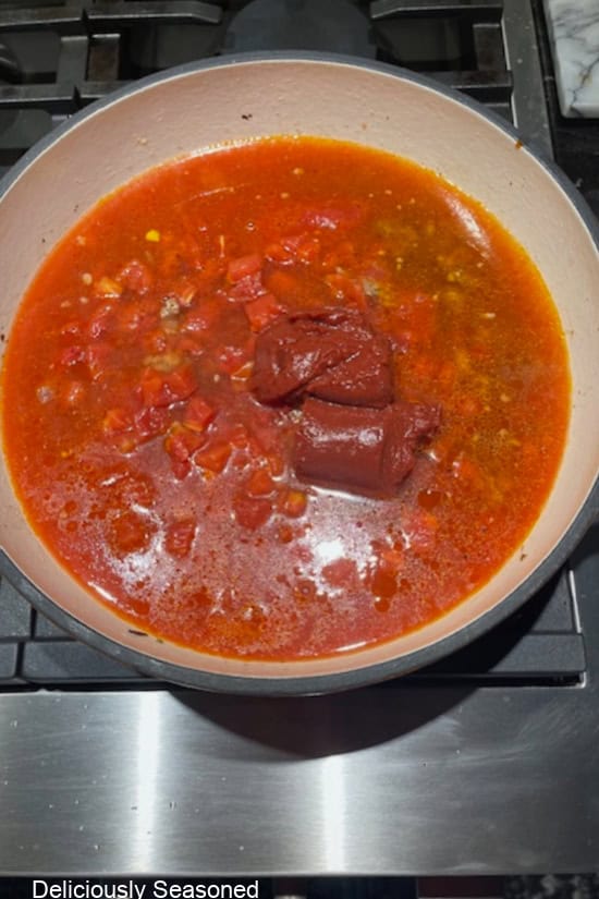 A cast-iron pot with the beef broth, water, and tomato sauce, paste, and diced tomatoes added.