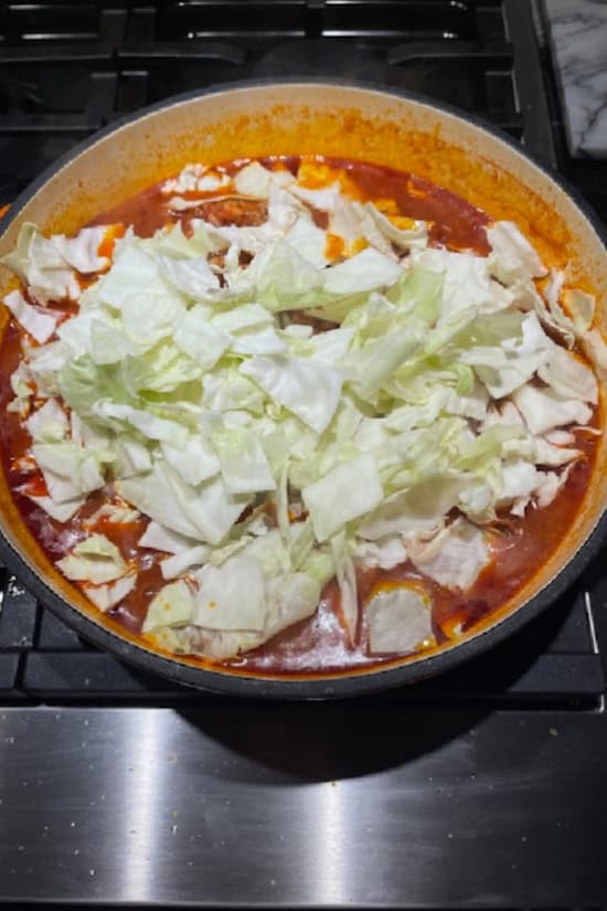 A cast-iron pot with cut cabbage added to the mixture before stirring it together.