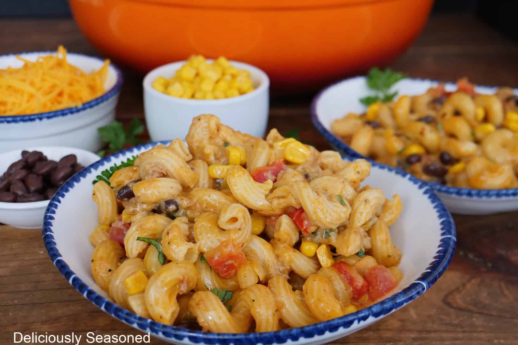 A wood surface with two white bowls with blue trim filled with a serving of chorizo pasta with southwest flavors.