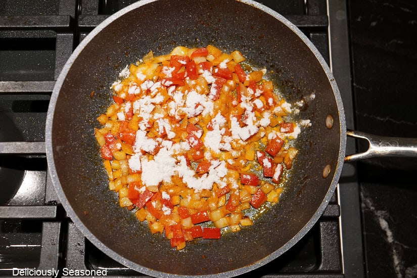A pan with cooked red bell peppers and onions in it with flour sprinkled over the veggies.