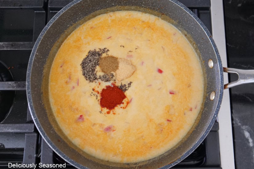 A pan with a cheesy sauce with different seasonings being added it the sauce.