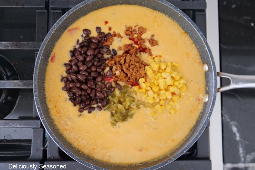 A pan with a cheesy cream sauce with black beans, corn, chorizo, diced green chilies added.