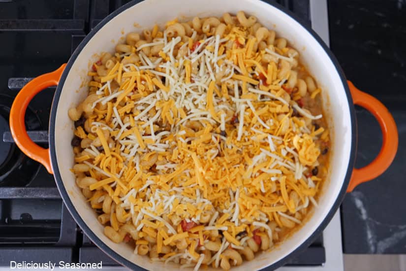 A pan with the noodles added and topped with two types of shredded cheeses on top.