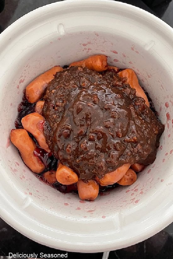 A white crockpot with grape jelly, bacon jam, and little smokies in it before being stirred together.