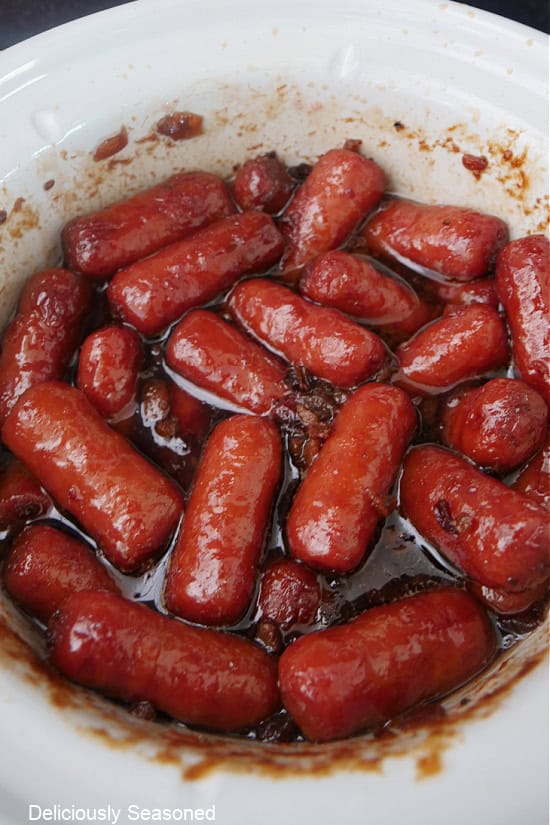 A white crockpot filled with slow cooked little smokies.