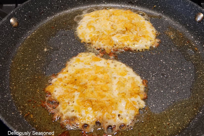 A frying pan with two cheesy shells cooking in the pan.
