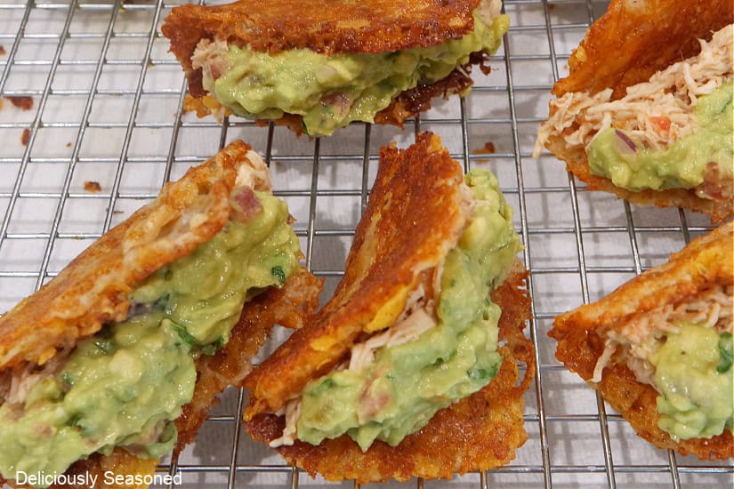 A wire rack with homemade crunchy cheese shells filled with shredded chicken and topped with guacamole.