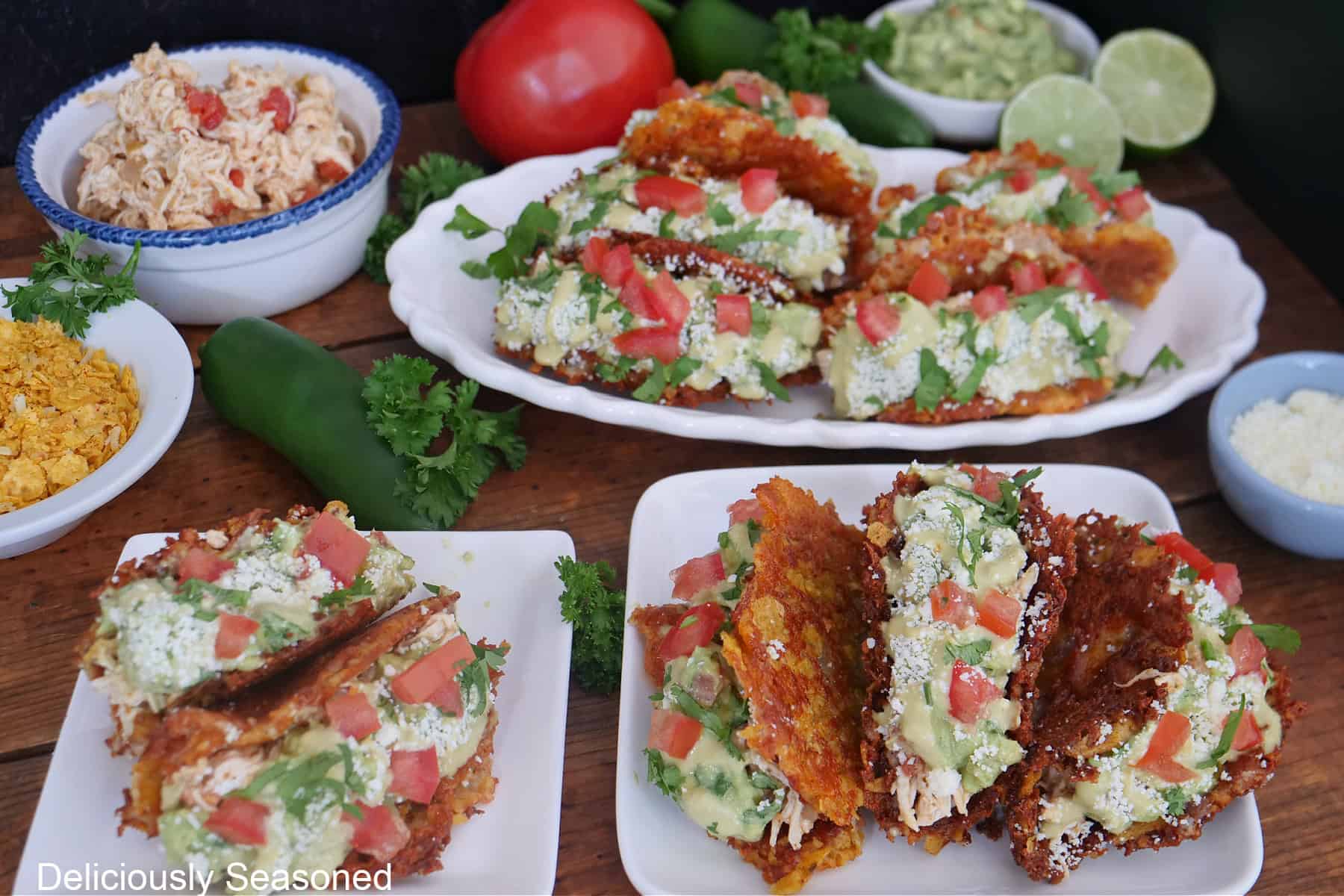 A wood surface with three white plates with crunchy Doritos chicken tacos on them.