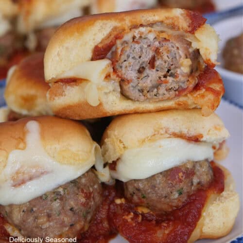Three mini turkey meatball sliders on a white plate with blue trim with a bite out of the slider on top.