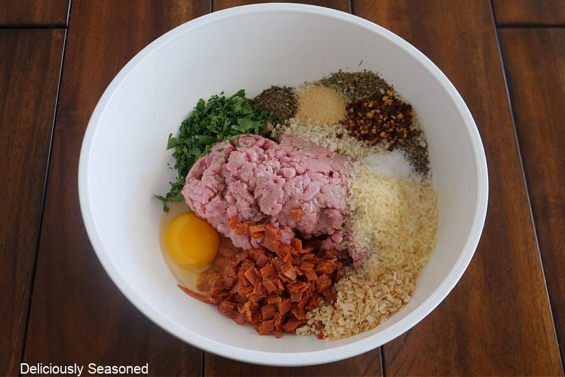 A wood surface with a white bowl filled with all the ingredients to make turkey meatballs being being mixed together.