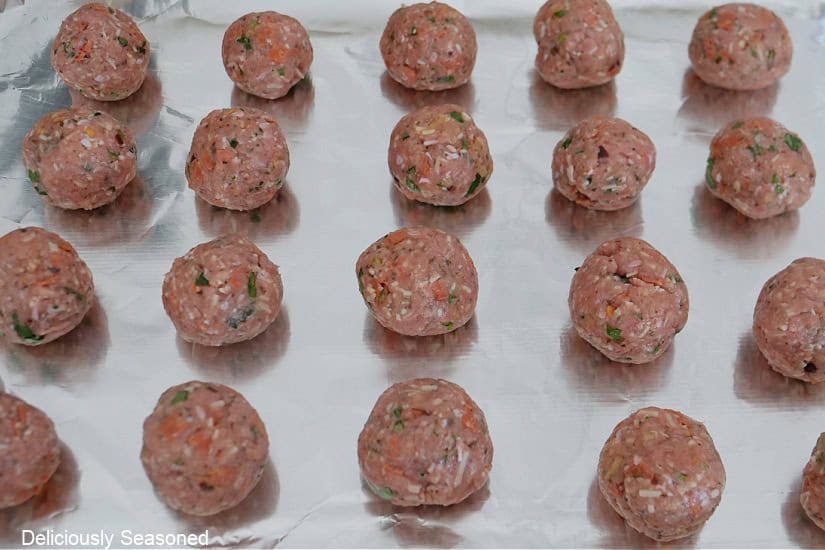 A foil lined baking sheet with turkey meatballs on it before being baked in the oven.