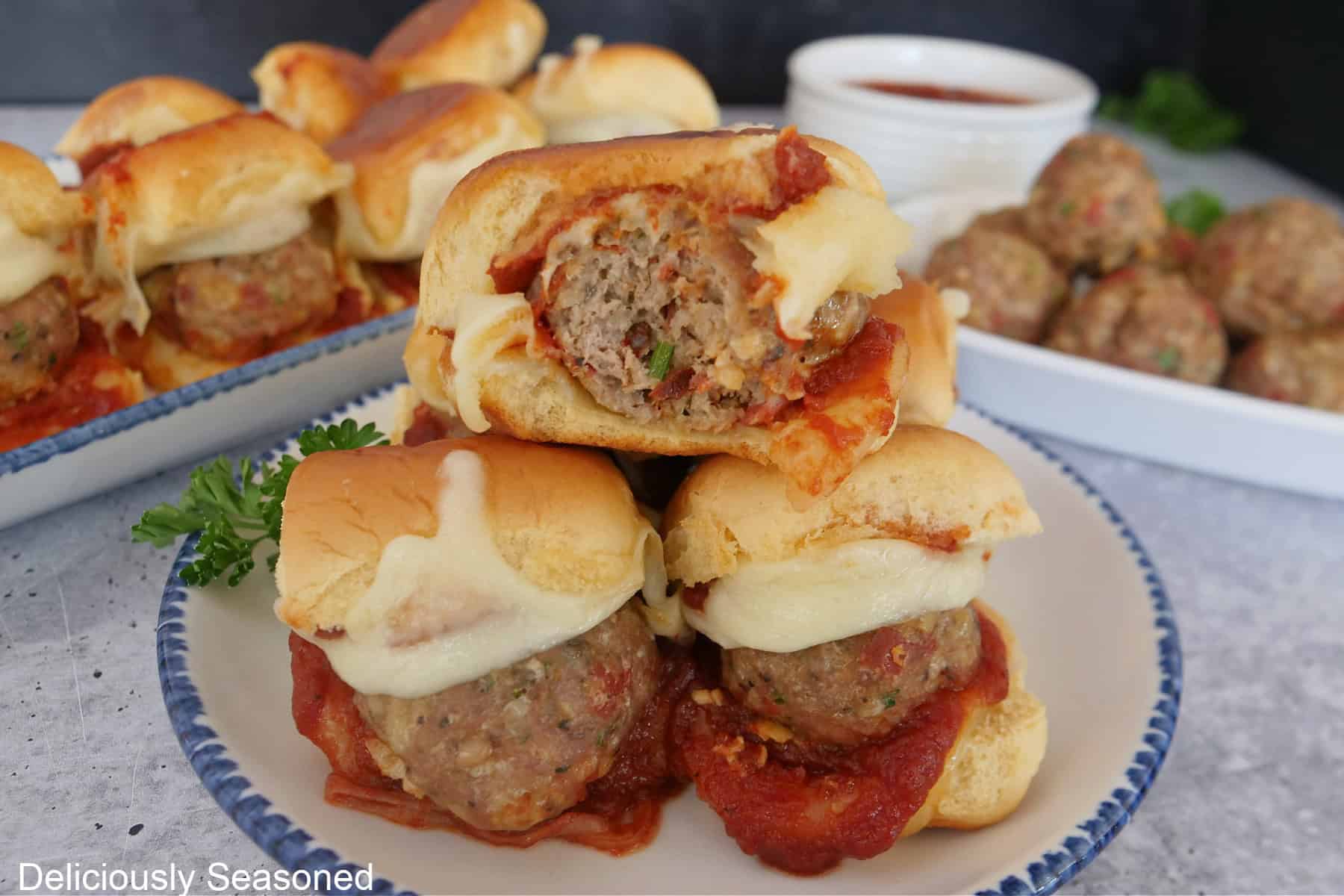 A grey surface with white plates with blue trim with mini turkey meatball sliders on them.