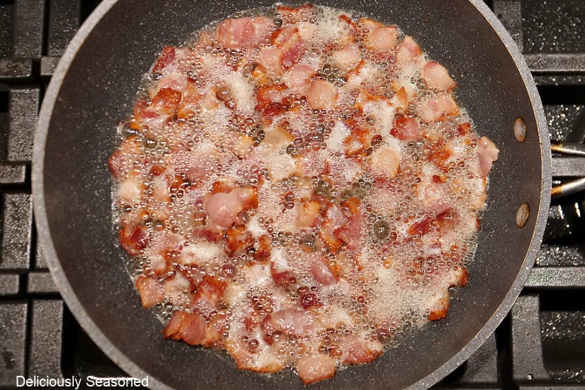 A frying pan with chopped bacon in it frying.