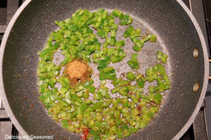 A frying pan with diced jalapenos and seasoning in it sautéing.