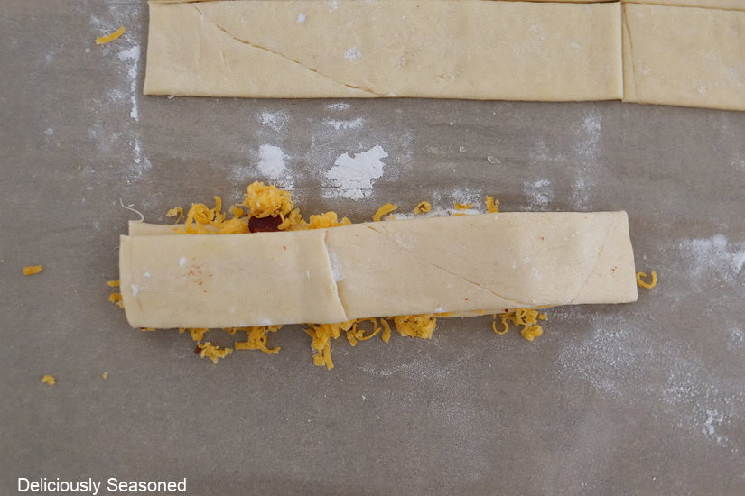 Two crescent dough strips with shredded cheese, jalapeno popper mix, and bacon inside before being twisted and placed on a baking sheet.
