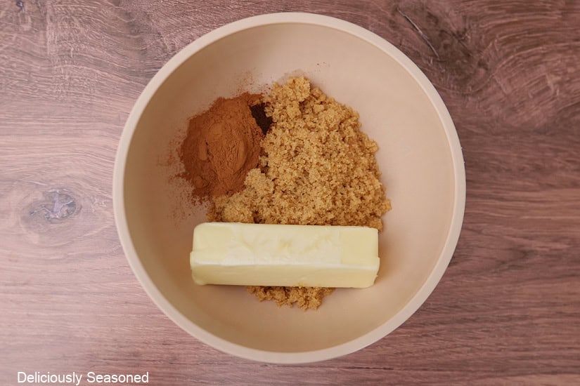 A wood surface with a light pink mixing bowl with the ingredients in it to make the cinnamon filling.