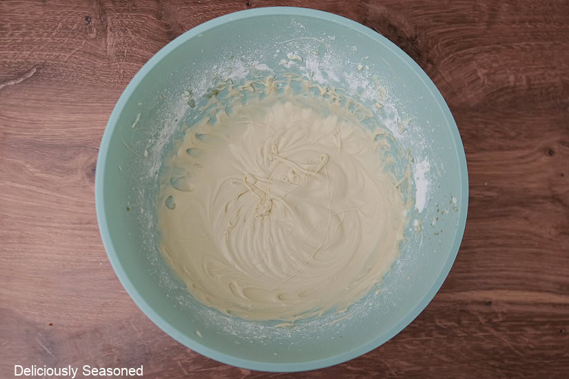 A wood surface with a light blue mixing bowl with the maple icing ingredients mixed together.