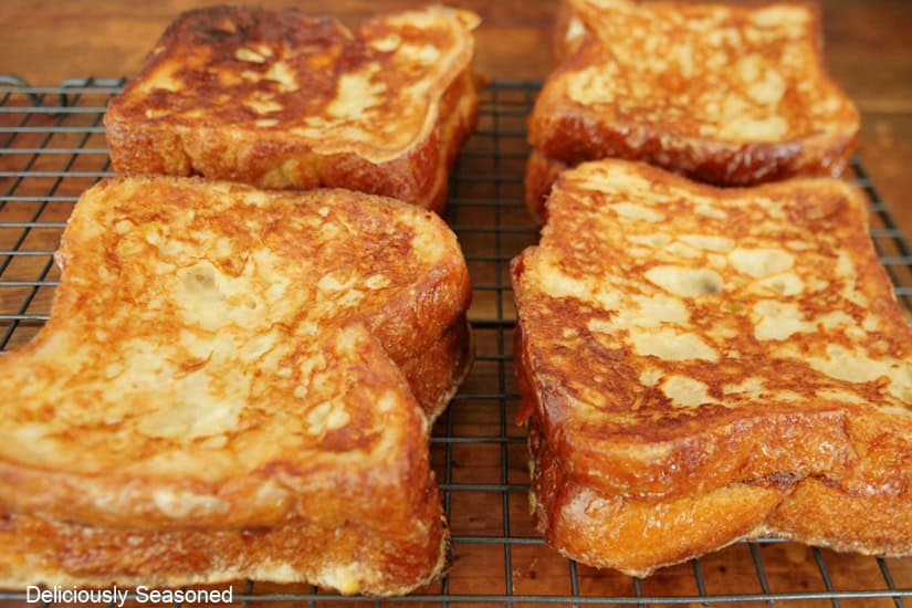 A wire rack with four cinnamon roll French toasts on it after being fried.