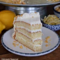 A round white plate with blue trim with a slice of lemon crunch layered cake on it.