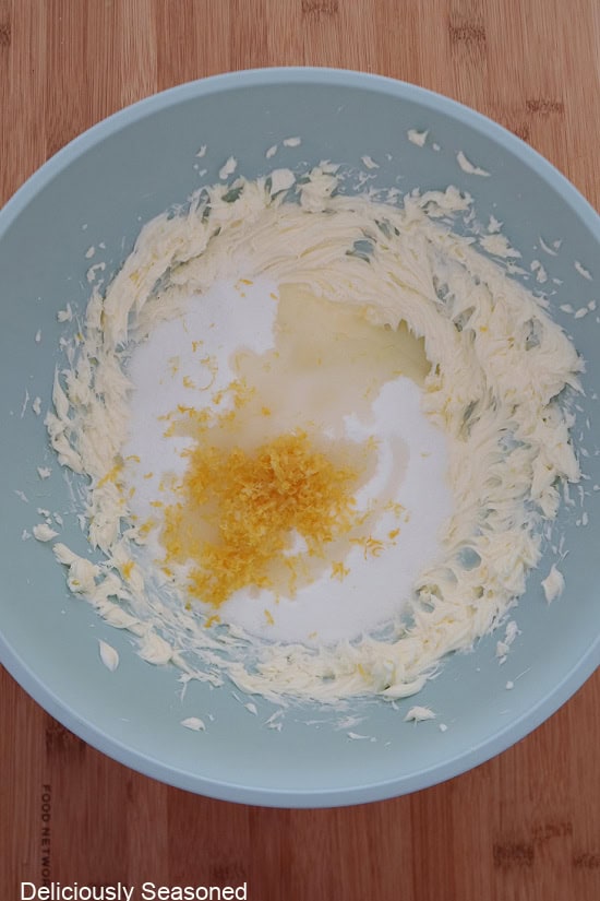 A light blue bowl with the wet ingredients in it showing the lemon zest on top before being mixed into the batter.