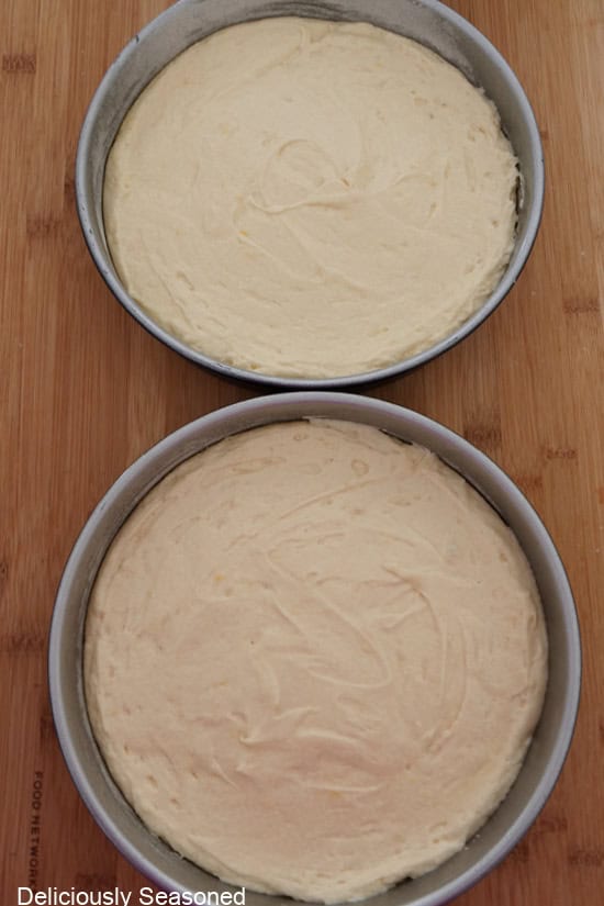 A wood surface with two round baking pan filled with lemon cake batter being being baked.