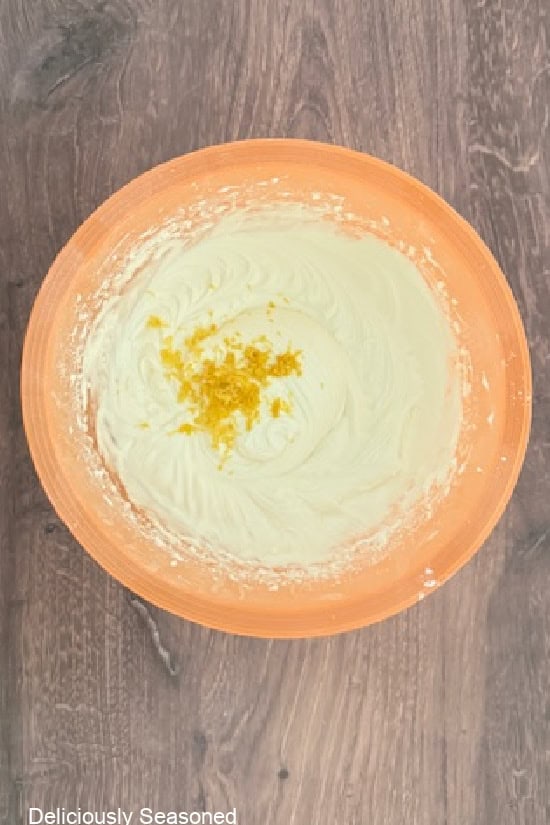 A light orange mixing bowl with lemon zest about to be mixed into the lemon cream cheese frosting.